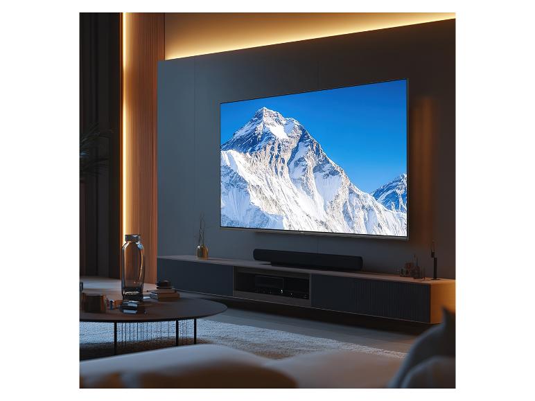 Grand téléviseur à écran plat fixé au mur, affichant une montagne enneigée, dans un salon moderne.