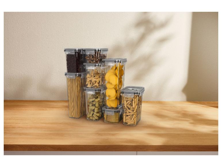 Contenants alimentaires transparents remplis de pâtes, de noix et de grains de café sur une table en bois.