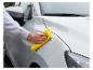Personne nettoyant une voiture blanche avec un chiffon microfibre jaune.