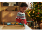 Enfant souriant joue avec un train en bois, sapin de Noël illuminé en arrière-plan.