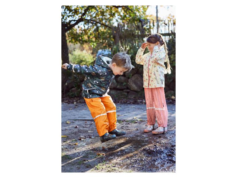 Deux enfants en vêtements de pluie jouent dans une flaque de boue.