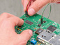 Une main connecte des fils à un circuit imprimé avec une puce intégrée.
