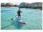Homme faisant du paddleboard dans des eaux turquoise avec une côte rocheuse en arrière-plan.