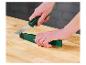 Des mains tiennent un couteau avec un manche vert et noir et un étui vert sur une table en bois.