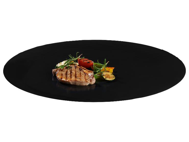 Côtelette de porc grillée avec légumes grillés et romarin sur une assiette noire.