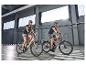 Deux personnes casquées et en tenue de sport à vélo électrique dans un parking intérieur.