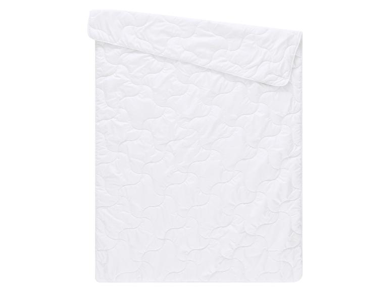 Couverture matelassée blanche avec motif ondulé, pliée sur le dessus.