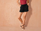 Shorts noirs à dentelle et espadrilles sur un fond beige.