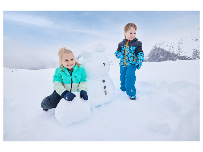 Deux enfants en vêtements d'hiver construisent un bonhomme de neige dans la neige.