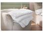Pile de couettes blanches sur un fauteuil beige dans une chambre.