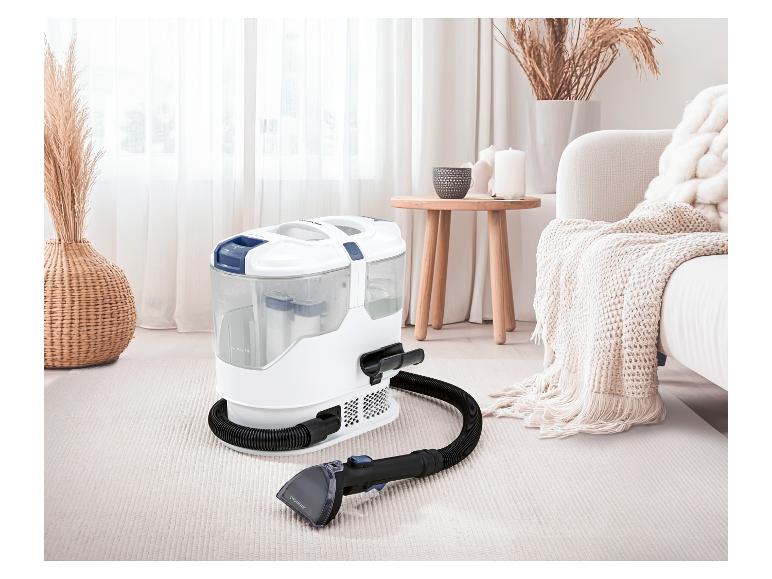 Nettoyeur de tapis avec tuyau et buse sur un tapis clair dans un salon confortable.