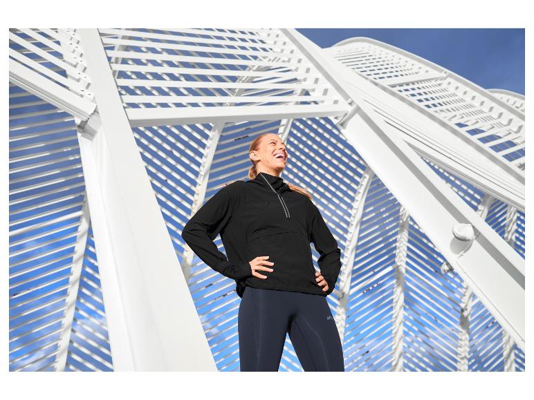 Femme en haut de sport noir et leggings, souriante devant une architecture blanche.