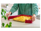 Une femme retire un plat cuit au four d'un moule rouge Coox.