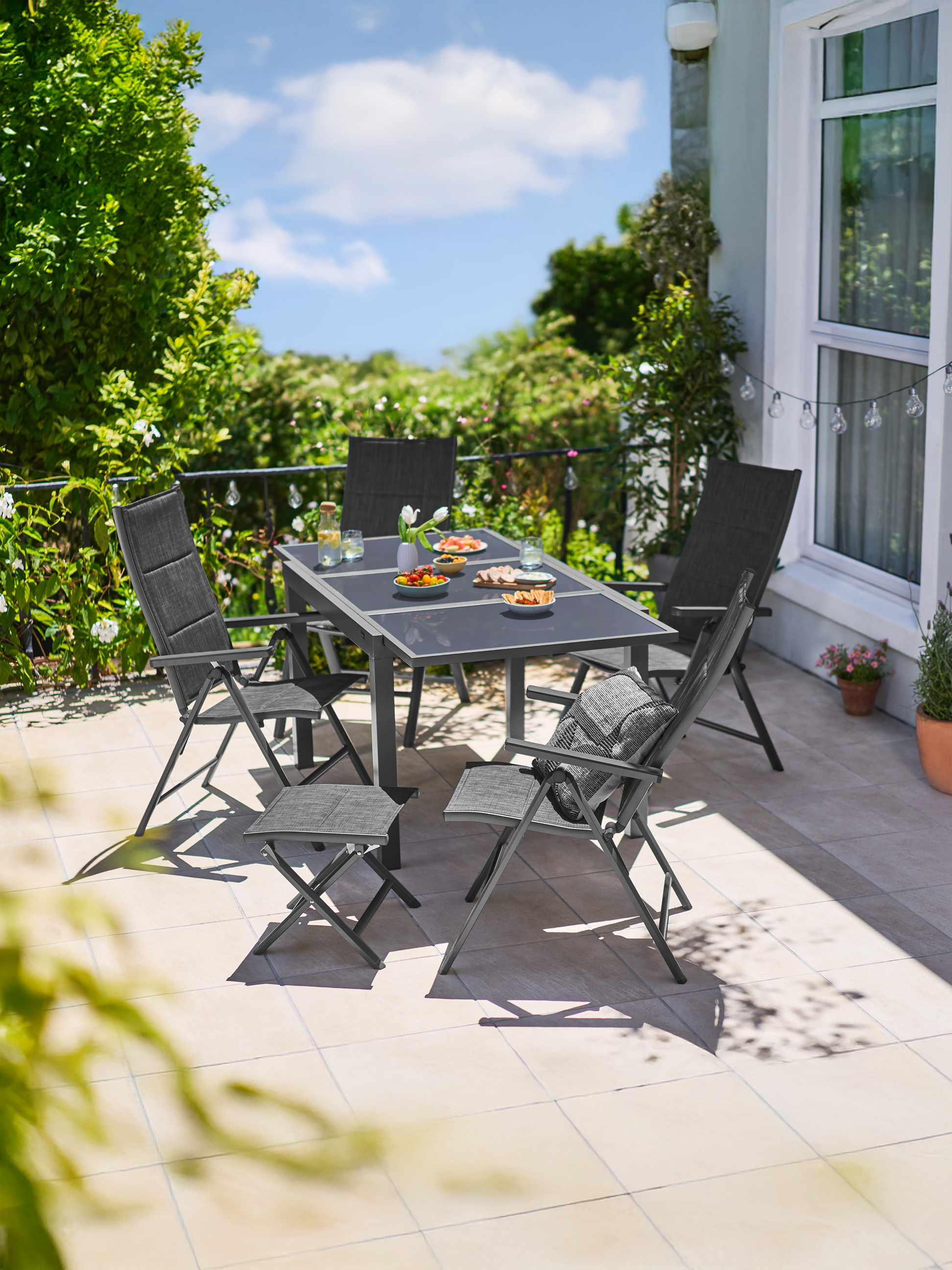 Ensemble de salle à manger d'extérieur avec table et chaises grises sur une terrasse, entouré de verdure luxuriante.