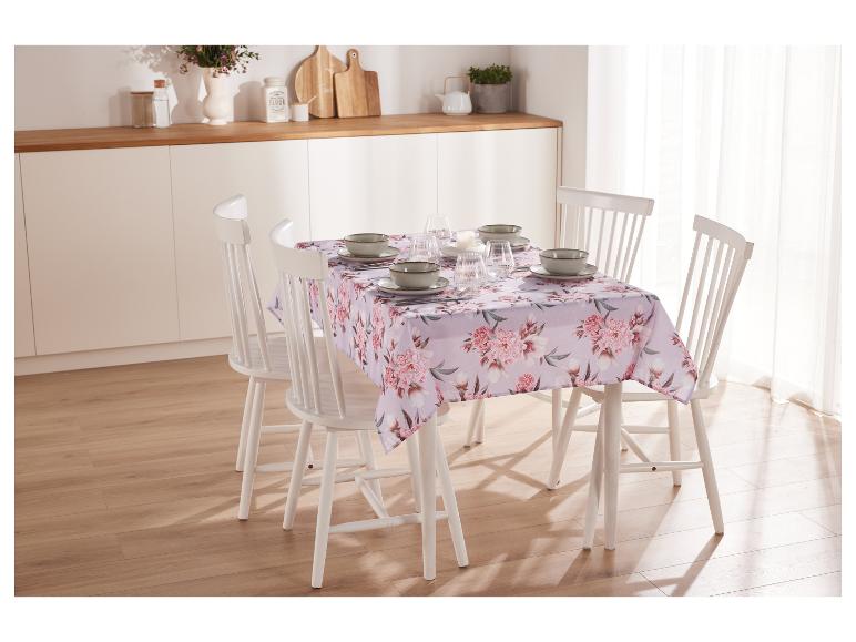 Une table avec une nappe fleurie et des chaises blanches dans une salle à manger lumineuse.