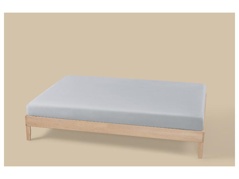 Lit avec cadre en bois clair et matelas gris sur fond beige.