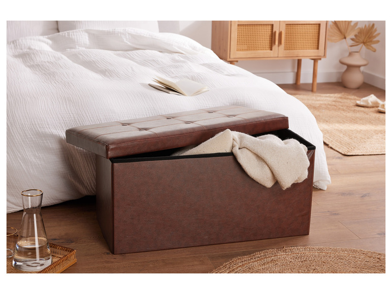 Un coffre de rangement en cuir marron avec un couvercle, ouvert avec une couverture blanche à l'intérieur.