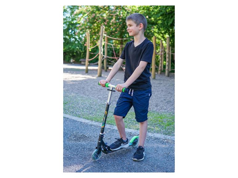Garçon avec une trottinette noire et verte dans une aire de jeux.