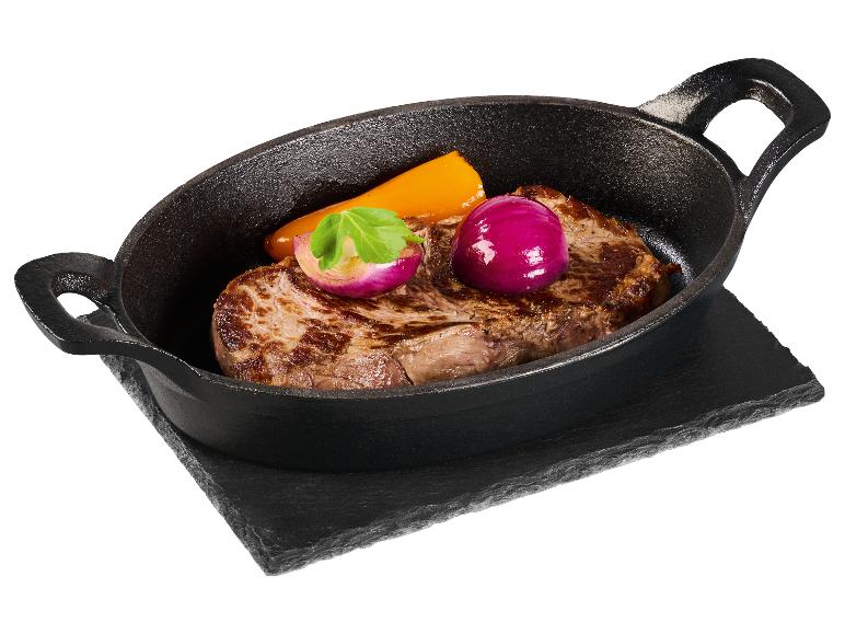 Steak, oignons rouges et carottes dans un plat en fonte.