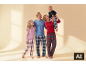 Famille souriante en pyjamas à carreaux, le père et la fille regardant la mère qui tient un bébé rieur.