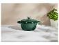 Une cocotte en fonte verte avec couvercle sur une surface en marbre blanc, à côté d'un plant de basilic.