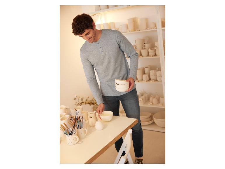Un homme examine des bols blancs et d'autres céramiques dans un magasin.