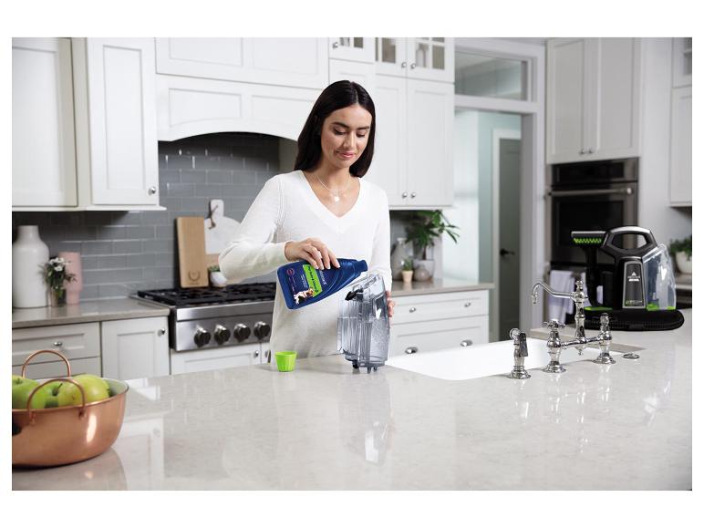 Femme versant du liquide détachant pour animaux de compagnie dans un nettoyeur portable dans la cuisine.