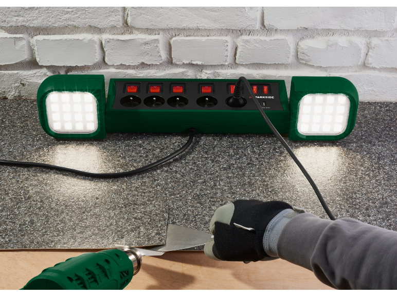 Multiprise verte avec lumières et une personne utilisant un pistolet thermique et un grattoir.