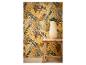 Tabouret en bois avec un vase de verdure devant un papier peint jaune à feuilles tropicales.