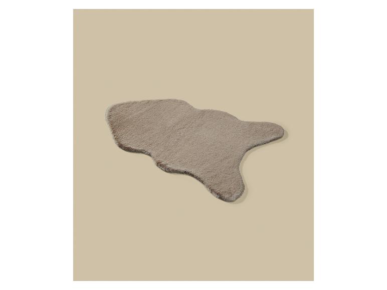 Un tapis en fausse fourrure beige de forme irrégulière sur un fond beige.