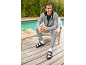 Homme en survêtement gris et sandales noires avec chaussettes blanches, souriant et tenant un smoothie vert.