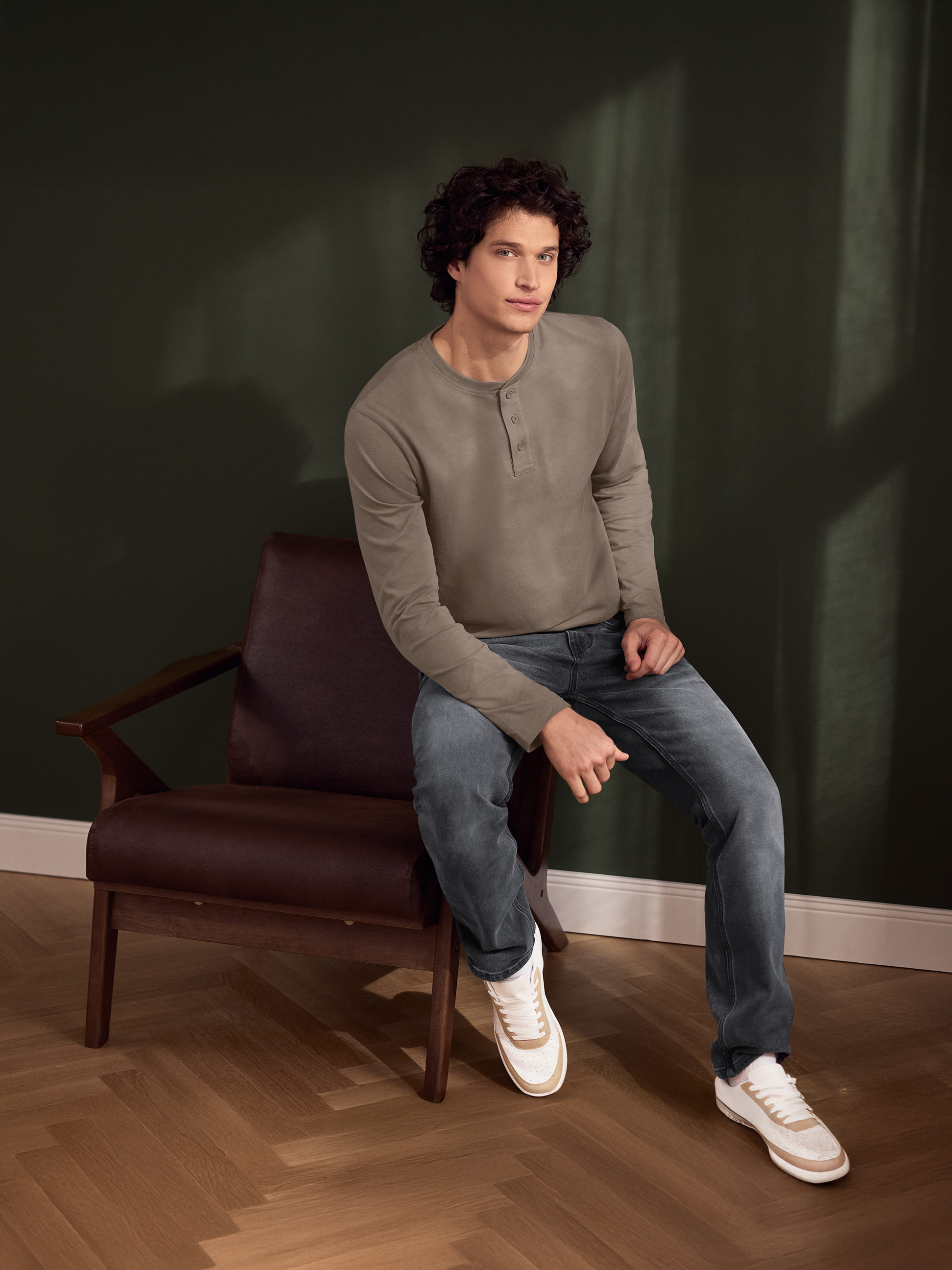 Homme en chemise Henley marron et jean assis sur un fauteuil en cuir.