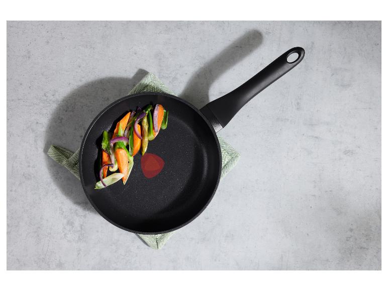 Poêle noire avec des légumes coupés (carottes, oignons, asperges) sur un torchon vert.