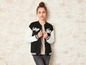 Une femme porte une veste varsity noire avec des manches blanches et l'inscription 'College' et 'Team'.