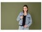 Une femme en jean et veste en jean pose devant un fond vert.