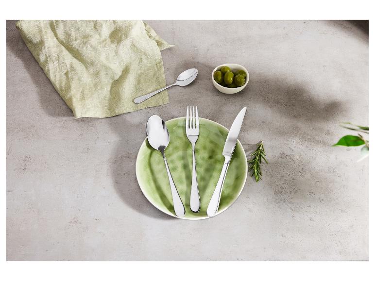 Ensemble de couverts avec assiette, serviette et olives sur fond gris.