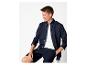 Homme en chemise bleu marine, t-shirt blanc et short bleu marine, assis sur un tabouret.