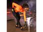 Une femme vêtue d'un haut orange et d'un pantalon de jogging noir s'étire dans un environnement urbain.