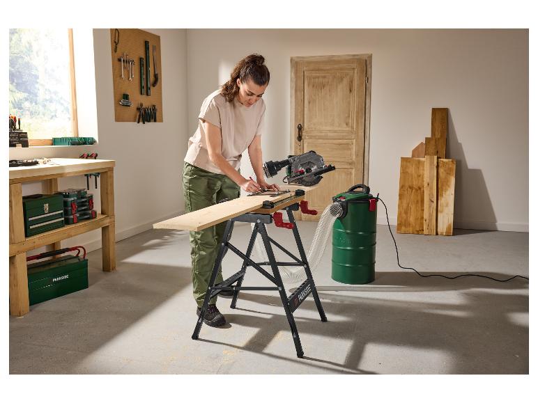 Femme utilise une scie circulaire et un aspirateur industriel pour couper du bois dans un atelier.
