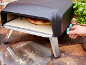 Four à pizza compact avec une pizza en cuisson et une main ajustant les cadrans, sur une table en bois.