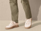Des baskets blanches avec une semelle marron, portées avec un pantalon vert.