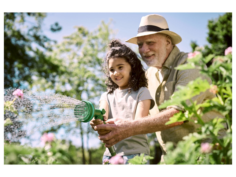 Un homme et une fille arrosent des plantes dans le jardin avec un tuyau d'arrosage vert.