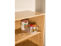 Organisateur transparent avec des pâtes penne et deux pots d'épices sur une étagère en bois.
