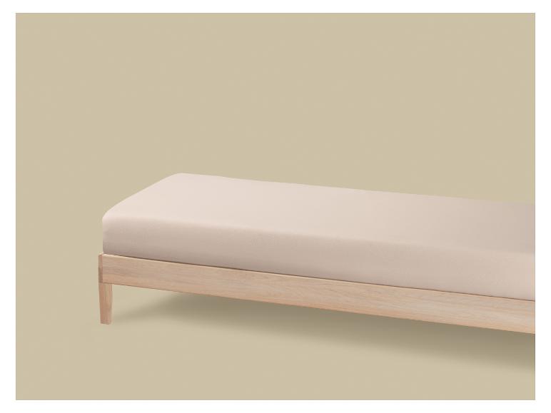 Un lit en bois clair avec un matelas beige, sur un fond beige.