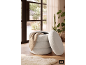 Pouf de rangement bouclé blanc avec couverture, près d'une fenêtre donnant sur un jardin.
