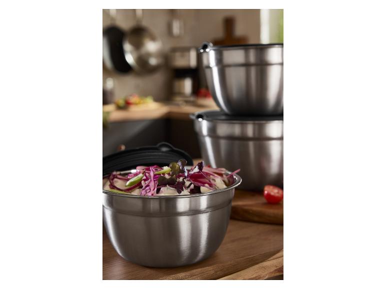 Bols mélangeurs en acier inoxydable avec couvercles, l'un rempli de salade, dans une cuisine.