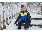 Enfant souriant en veste de ski et pantalon de neige assis sur des marches enneigées.