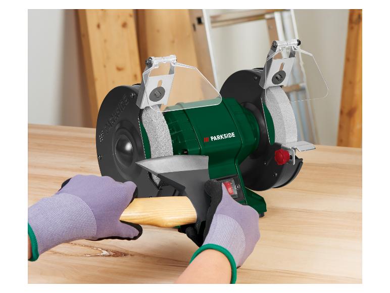 Meuleuse d'établi Parkside affûtant une hache, avec des mains gantées.