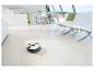 Aspirateur robot nettoyant le sol dans un salon moderne où une femme travaille sur un ordinateur portable.