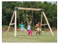 Enfants jouant sur une balançoire en bois et des anneaux de gymnastique dans un jardin.